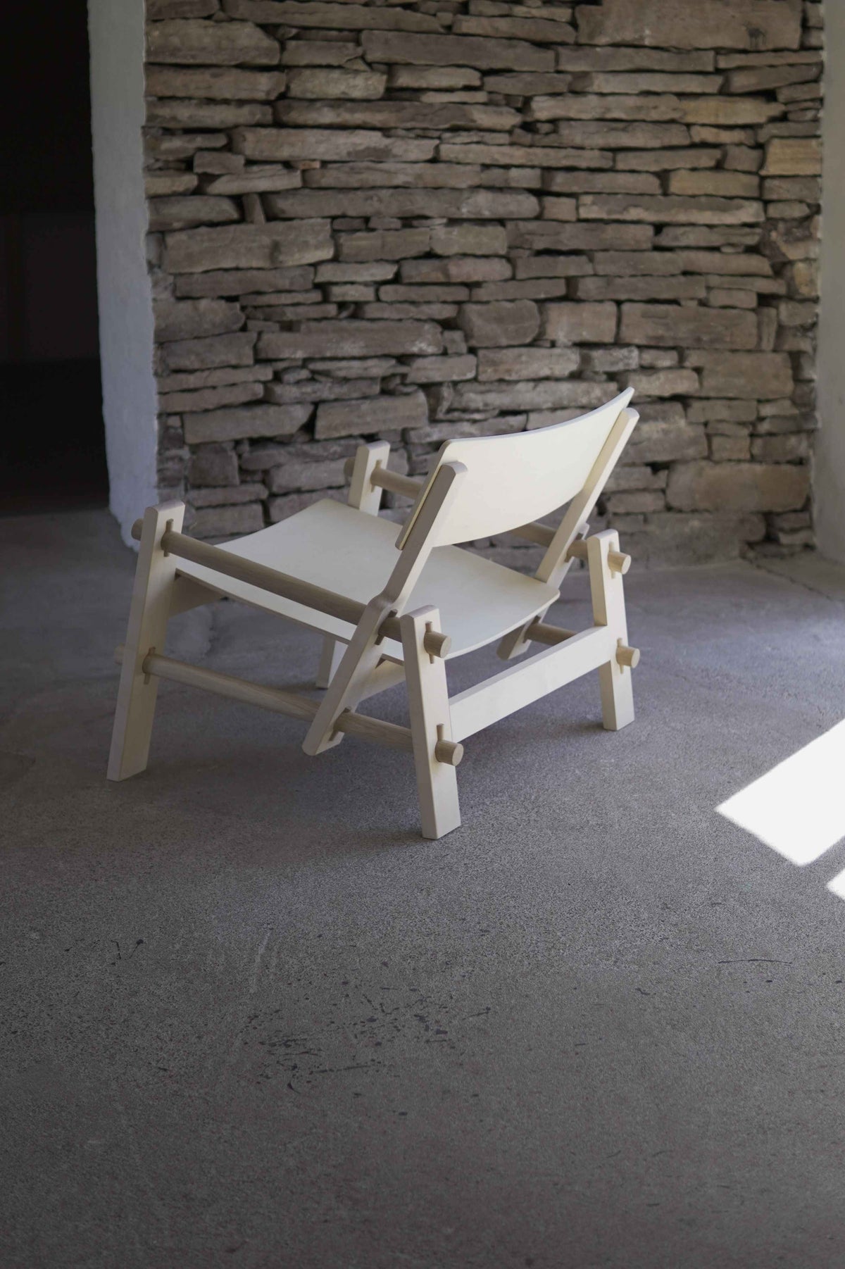 White chair against a stone wall in a room with concrete floor